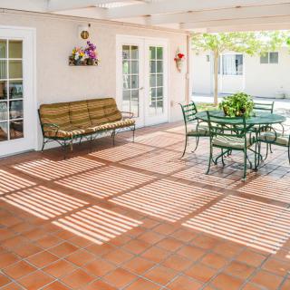 A sunny patio with terracotta tiles, featuring a bench, table and chairs, and decorative plants.