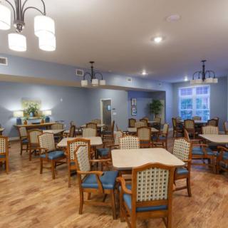 A spacious dining area with wooden tables and chairs, featuring elegant lighting and a wood floor.