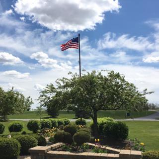 An American flag flies over a beautifully maintained garden with clear skies and scattered clouds.