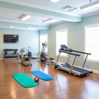 A small home gym with exercise equipment including a treadmill, elliptical, weights, and yoga mats.