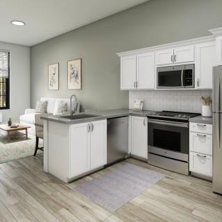 A modern open-concept kitchen with white cabinets, stainless steel appliances, and wood flooring flows into a cozy living area.