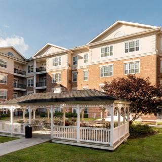 A residential apartment building with a wooden gazebo in the foreground and well-maintained landscaping.
