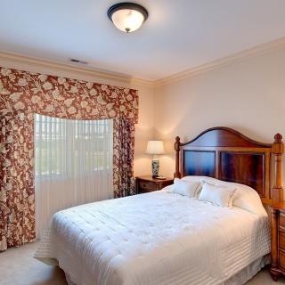 A cozy bedroom with a wooden headboard, patterned curtains, and a bedside lamp.