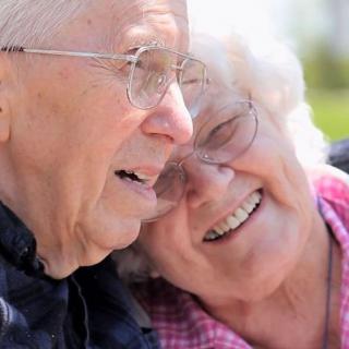 An elderly couple sharing a joyful moment outdoors, embracing each other warmly.