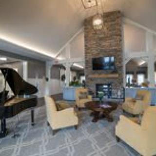 A modern living room featuring a grand piano, cozy seating area, and a stone fireplace under a high vaulted ceiling.
