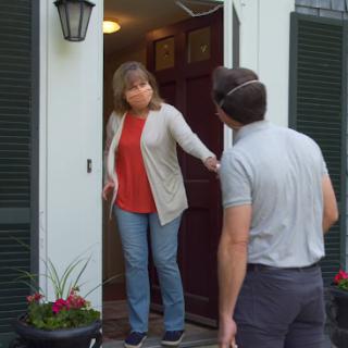 A friendly home visit, where one person arrives at a door to greet another.