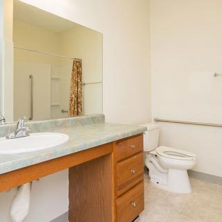 A clean and spacious bathroom with a large mirror, sink, and toilet.