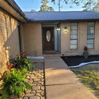 A welcoming entrance of a brick house with a walkway and surrounding plants.