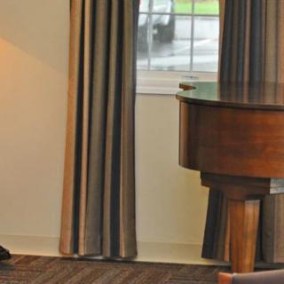A cozy interior scene featuring a grand piano next to a window with curtains and a floor lamp.
