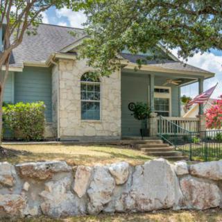 A charming house with a stone facade and a front porch, surrounded by greenery and a stone wall.