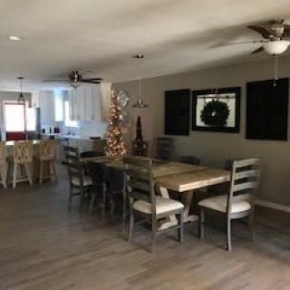 A spacious open-concept home interior featuring a dining area with a wooden table and chairs, a Christmas tree with holiday decorations, and an adjacent kitchen.