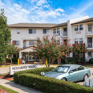 A multi-story apartment building with a car parked in front and trees lining the entrance.