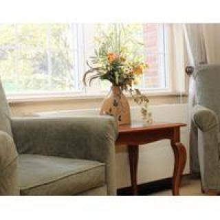 A cozy living room with armchairs and a small table adorned with a vase of flowers next to a bright window.