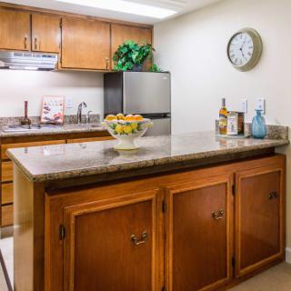 A cozy kitchen with wooden cabinets and a granite countertop, featuring an island centerpiece adorned with fresh fruits and wine bottles.