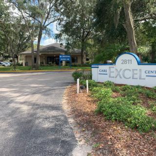 Entrance to a facility with a sign labeled 'EXCEL' amid lush greenery.