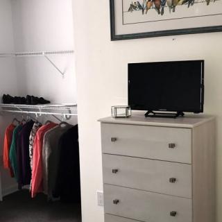 A bedroom with a dresser and television next to an open closet filled with clothes.