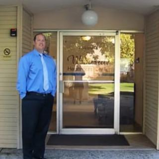 A man in business attire stands in front of a building entrance with glass doors.