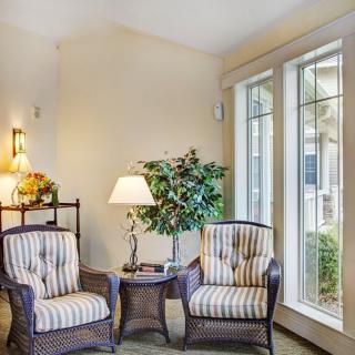 A cozy living room corner with two striped armchairs, a lamp, and large windows.