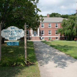 A brick building with a sign in front, surrounded by grass and trees.