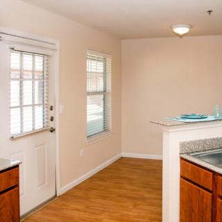 A simple kitchen interior with wooden floors, cabinets, a window, and a door.