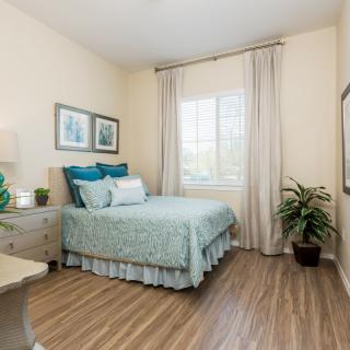 A cozy bedroom with soft lighting, featuring a neatly made bed, wooden flooring, and decorative plants.