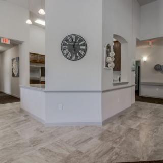 A modern lobby with a reception area featuring white walls and tile flooring, decorated with a wall clock.