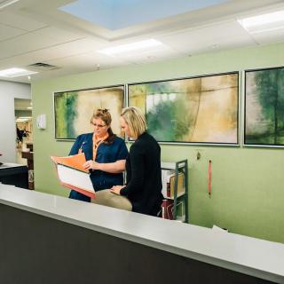 Two people engaged in discussion at an office desk, reviewing documents.