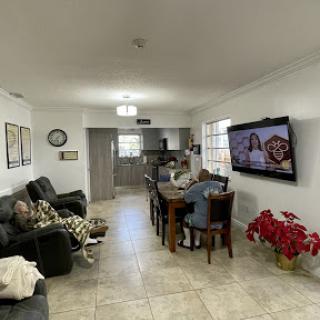 A cozy living room setting with a family gathered around the dining table and watching TV.