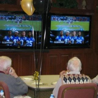 A group of seniors watching a football game on two televisions, with balloons celebrating the occasion.