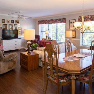 A cozy living and dining area featuring elegant wooden furniture, a television, and large windows providing natural light.