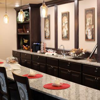 A modern kitchen interior featuring a long countertop with seating, pendant lights, and decorative artwork on the wall.