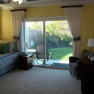A cozy bedroom features a sliding glass door opening to a backyard, with elegant curtains and comfortable furnishings.