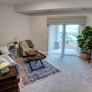 A cozy living room with a sofa, coffee table, and indoor plants, featuring a large window with curtains looking outwards.