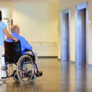 A nurse assisting a patient in a wheelchair down a hospital hallway.