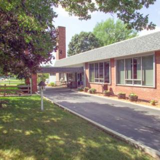A brick building with a driveway and surrounding trees on a sunny day.