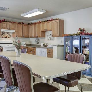 A cozy kitchen interior featuring a dining area with a large table and several chairs, surrounded by wooden cabinets and kitchen appliances.