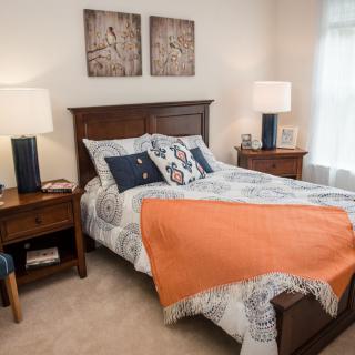A cozy bedroom with a neatly made bed, featuring patterned bedding and an orange blanket, flanked by wooden nightstands with lamps.