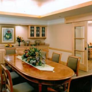 A well-furnished dining room featuring a large wooden table with chairs, decorated with a floral centerpiece and surrounded by artwork and cabinetry.