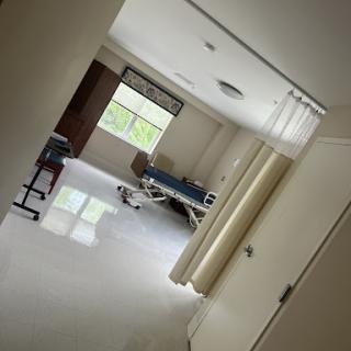 A view of a hospital room from the corridor, showcasing a patient bed and natural light coming through the window.