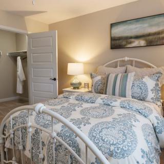 A cozy bedroom interior featuring a well-decorated bed with patterned bedding, a nightstand with a lamp, and artwork on the wall.