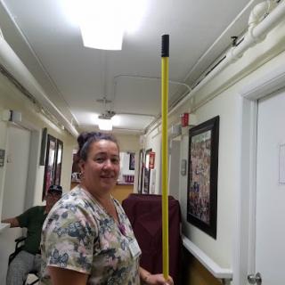 A woman holding a yellow cleaning pole stands in a hallway.