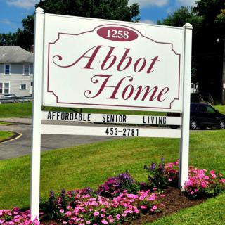 Sign for Abbot Home, a nursing and retirement community, with flowers in the foreground.