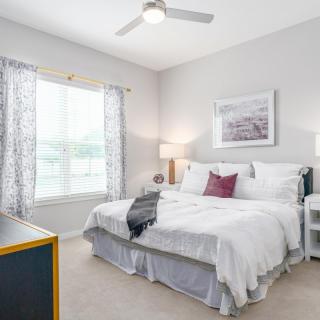 A bright and cozy bedroom with white bedding, nightstands, lamps, and a ceiling fan.