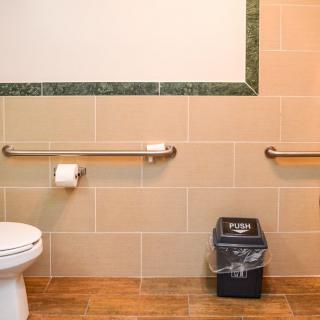 An accessible bathroom featuring handrails, a toilet, and a trash can.
