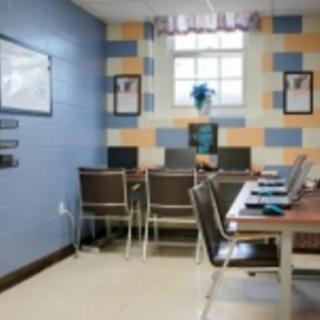 A small computer room with desks, chairs, and multiple computers lined against a wall with colorful tiles.