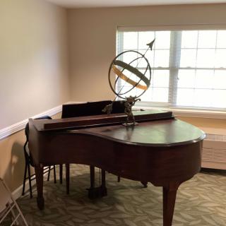 A grand piano in a well-lit room with a decorative sphere on top.