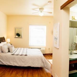 A cozy bedroom with a neatly made bed, hardwood floors, and an adjoining bathroom.