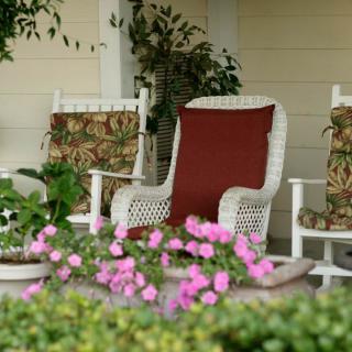 A cozy porch with wicker rocking chairs surrounded by lush greenery and vibrant pink flowers.