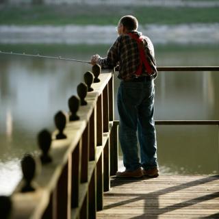 A man is fishing while standing on a dock by the lake.
