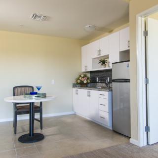 A small kitchen area with white cabinets, a stainless steel fridge, and a dining table with chairs.